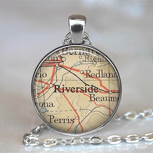May include: A round silver pendant necklace featuring a vintage-style map print under a glass dome. The map displays geographic locations including Riverside, Redlands, and Perris with black text and red road lines on a beige background.