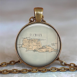May include: A round pendant necklace with a vintage map of St. Croix. The map is in shades of tan and brown, set against a light background. The pendant has a gold-colored frame and chain.