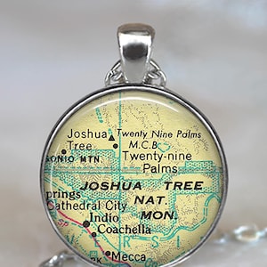 May include: Silver-toned pendant with a circular design featuring a map of Joshua Tree National Park. The map includes place names like Joshua Tree, Indio, and Coachella. The pendant hangs from a silver chain.