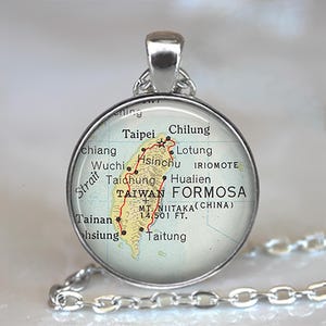 May include: A silver-toned pendant necklace featuring a circular charm with a map of Taiwan. The map is in shades of yellow, green, and red, with place names and the text "TAIWAN FORMOSA" visible. The chain is also silver.