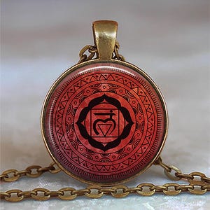 May include: A round pendant necklace with a bronze-colored chain. The pendant features a red and black chakra design with intricate patterns. The pendant is approximately 1.5 inches in diameter.