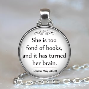May include: Silver pendant necklace with a circular, white pendant. The pendant displays the quote "She is too fond of books, and it has turned her brain." by Louisa May Alcott in black text. The chain is visible.