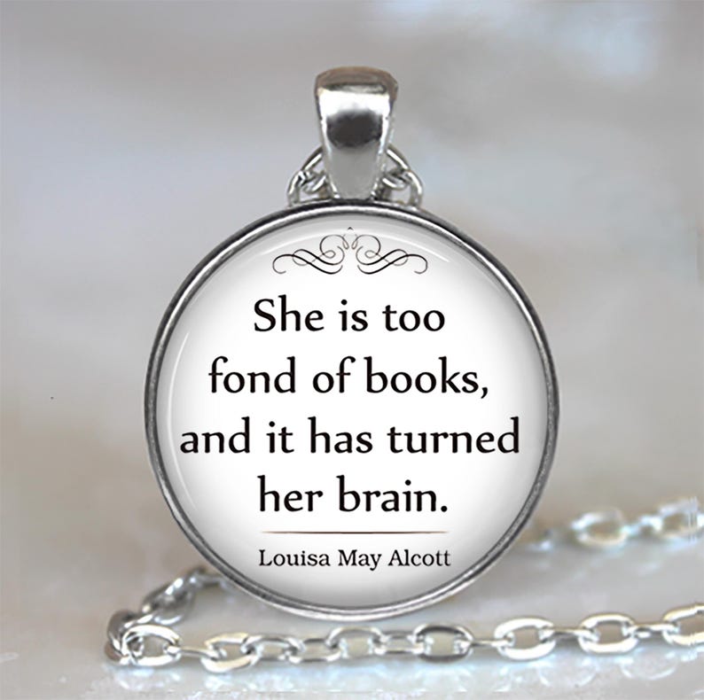 May include: Silver pendant necklace with a circular, white pendant. The pendant displays the quote "She is too fond of books, and it has turned her brain." by Louisa May Alcott in black text. The chain is visible.