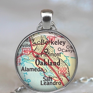 May include: A silver necklace with a round pendant featuring a vintage map of Oakland, California. The map shows the cities of Berkeley, Piedmont, Alameda, and San Leandro. The pendant is about 1 inch in diameter.