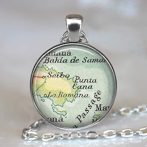 May include: A round silver pendant with a map design. The map features place names like "Bahia de Samaná" and "Punta Cana" in a vintage style. The pendant hangs from a silver chain.