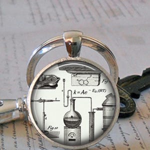 May include: A silver keychain with a round glass charm featuring a vintage scientific illustration of a laboratory setup with a flask, tubing, and the equation "k=Ae-Ea/(RT)".