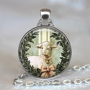 May include: Silver-toned pendant necklace featuring a round charm with a vintage illustration of a lamb. The lamb has a pink bow and a bell. The charm is surrounded by a green wreath design, and the background has a striped pattern.