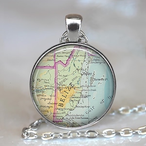 May include: A round silver pendant necklace featuring a map of Belize. The map is in shades of green, yellow, and pink, with the word "BELIZE" prominently displayed. The pendant hangs from a silver chain.