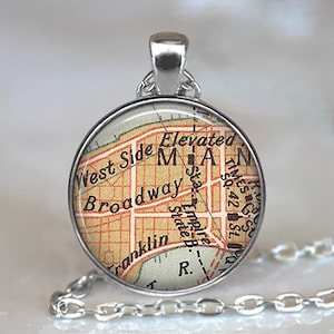 May include: A silver-toned pendant necklace featuring a circular charm with a vintage map design. The map includes the words "West Side," "Broadway," and "Empire State B." The pendant hangs from a delicate chain.