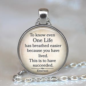 May include: A silver-toned pendant necklace with a round, cream-colored charm. The charm features the quote "To know even One Life has breathed easier because you have lived. This is to have succeeded." by Emerson.