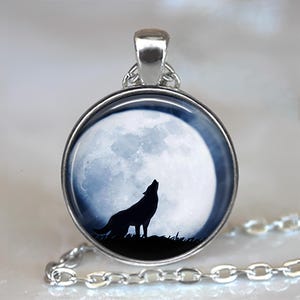 May include: Silver-toned pendant necklace featuring a round pendant with a wolf howling at the moon. The pendant has a black silhouette of a wolf against a large, bright, full moon. The chain is silver and has a link design.