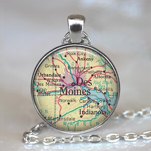 May include: A round silver pendant necklace featuring a vintage-style map of Des Moines, Iowa, and surrounding areas. The map displays city names like Ankeny, Indianola, and Urbandale with red and blue lines on a cream background under glass.