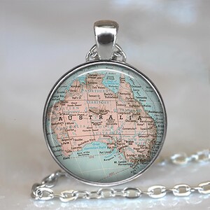 May include: A round silver pendant necklace featuring a vintage-style map of Australia under a clear glass dome. The map displays various cities, regions, and geographical features in shades of pale pink, tan, and light blue with black text.