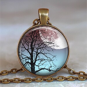 K&ouml;nnte beinhalten: Eine bronzene Halskette mit einem runden Glasanh&auml;nger, der eine Silhouette eines Baumes vor einem rosa und blauen Mond zeigt.