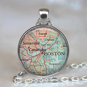 May include: Silver-toned pendant necklace featuring a circular pendant with a map of Boston. The map includes city names like Cambridge, Somerville, and Boston Harbor. The pendant hangs from a silver chain.