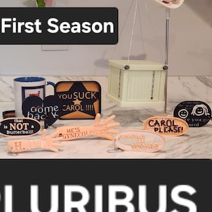 May include: A collection of novelty items, including a mug, signs, and a scale. The signs feature phrases like "YOU SUCK CAROL!!!!" and "CAROL PLEASE!". The text "Entire First Season" and "PLURIBUS" are also visible.