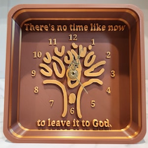Pode incluir: Relógio quadrado castanho com um desenho de árvore e as palavras "There's no time like now to leave it to God." O relógio tem ponteiros e números dourados. O relógio tem cerca de 25 cm quadrados.