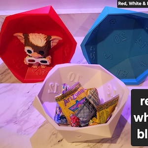 Puede incluir: Tres recipientes geométricos en rojo, blanco y azul. El recipiente rojo contiene una figura con gafas 3D. El recipiente blanco está lleno de bocadillos. El recipiente azul es un dado grande. El texto de la imagen dice "Red, White & Blue 3 pack".