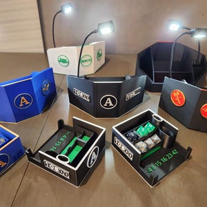 May include: An assortment of black, blue, and white tabletop gaming accessories, including dice trays, player screens, and storage boxes. Some items feature the letter "A" or the text "10800". Each item is illuminated by a small adjustable LED lamp.