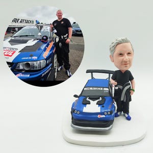May include: A custom figurine of a man in racing attire, standing next to a blue and white race car. The car has sponsor logos and the number 234. The figurine is on a white base.