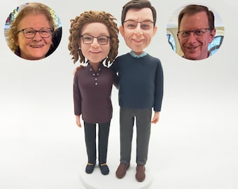 Puede incluir: Una figura de bobblehead personalizada de una pareja, con dos fotos de retrato adicionales en el fondo. La pareja viste ropa informal. La mujer lleva un suéter burdeos y pantalones negros, y el hombre un suéter azul marino y pantalones grises. La figura está sobre una base blanca.
