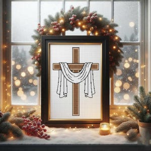 May include: A framed cross-stitch artwork featuring a brown cross draped with a white cloth. The artwork is set against a white background and framed in black with a gold inner border. The scene is decorated with a festive wreath and lights.