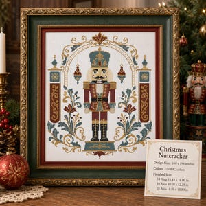 May include: A framed cross-stitch pattern of a nutcracker in a blue hat and red uniform, surrounded by ornate floral motifs and hanging ornaments. A card displays the text: Christmas Nutcracker, Design Size: 160 x 196 stitches, 22 DMC colors.