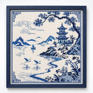 May include: A framed cross-stitch embroidery featuring a blue and white landscape scene with a pagoda, a pine tree, mountains, a small boat on water, and two flying birds. The design is enclosed in a geometric border within a dark blue frame.