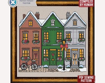 May include: Cross-stitch pattern of three colorful houses with snow-covered roofs and festive decorations. A bicycle is parked in front of the first house. The text "B&W And Colored Pattern" and "PDF SEWING PATTERN" are visible.