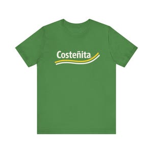 May include: Green t-shirt with the word "Costeñita" in white, arched above a yellow and white curved stripe. The t-shirt is a solid green color and has short sleeves.