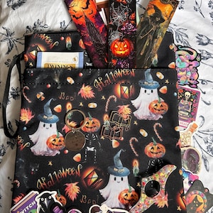 May include: Black Halloween-themed tote bag filled with bookmarks, stickers, and a tea bag. The bag features ghosts, pumpkins, and the word "Halloween." Bookmarks depict spooky scenes. Stickers include a witch, raven, and other Halloween-related designs.