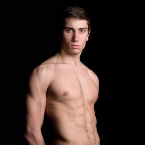 Puede incluir: Una persona sin camisa con un físico musculoso se encuentra frente a un fondo negro. La persona tiene el pelo castaño corto y mira a la cámara. La iluminación resalta el físico.