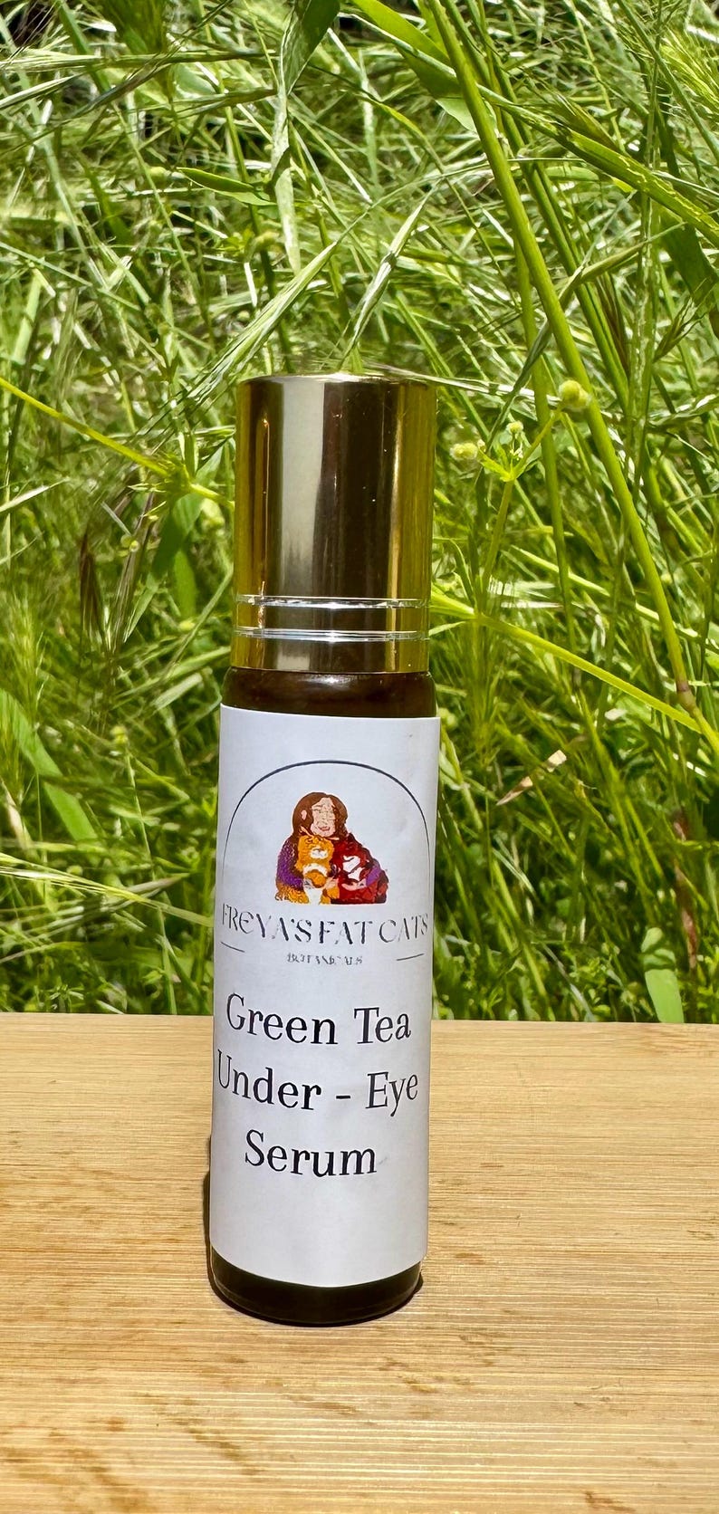 Peut inclure: Un flacon de roll-on dor&eacute; et blanc avec une &eacute;tiquette qui indique "FREYA'S FAT CATS BOTANICALS" et "Green Tea Under-Eye Serum".