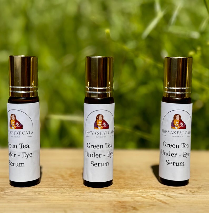 Peut inclure: Trois flacons roulants en verre dor&eacute;s et bruns avec des &eacute;tiquettes blanches. Les &eacute;tiquettes portent le texte "FREYAS FAT CATS" et "Green Tea Under - Eye Serum".
