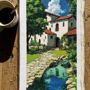 May include: Cross-stitch embroidery of a Mediterranean villa scene with a stone path, a stream, and lush greenery. The villa has white walls and a red tile roof. A cup of coffee sits on a wooden surface.