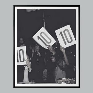 Puede incluir: Fotografía en blanco y negro de un grupo de personas sosteniendo carteles con el número 10. La imagen está tomada en interiores, con un fondo oscuro. Los carteles son blancos con números negros grandes, y la gente sonríe.