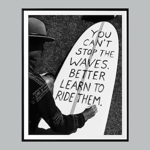 May include: Monochrome framed print showing a person with a surfboard. The surfboard displays the handwritten text: "You can't stop the waves. Better learn to ride them." The image is in black and white.