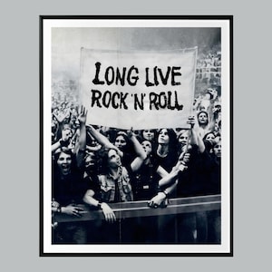 May include: Black and white photograph of a crowd at a rock concert. A banner reading "LONG LIVE ROCK 'N ROLL" is held aloft. The audience is enthusiastically raising their hands in the air.