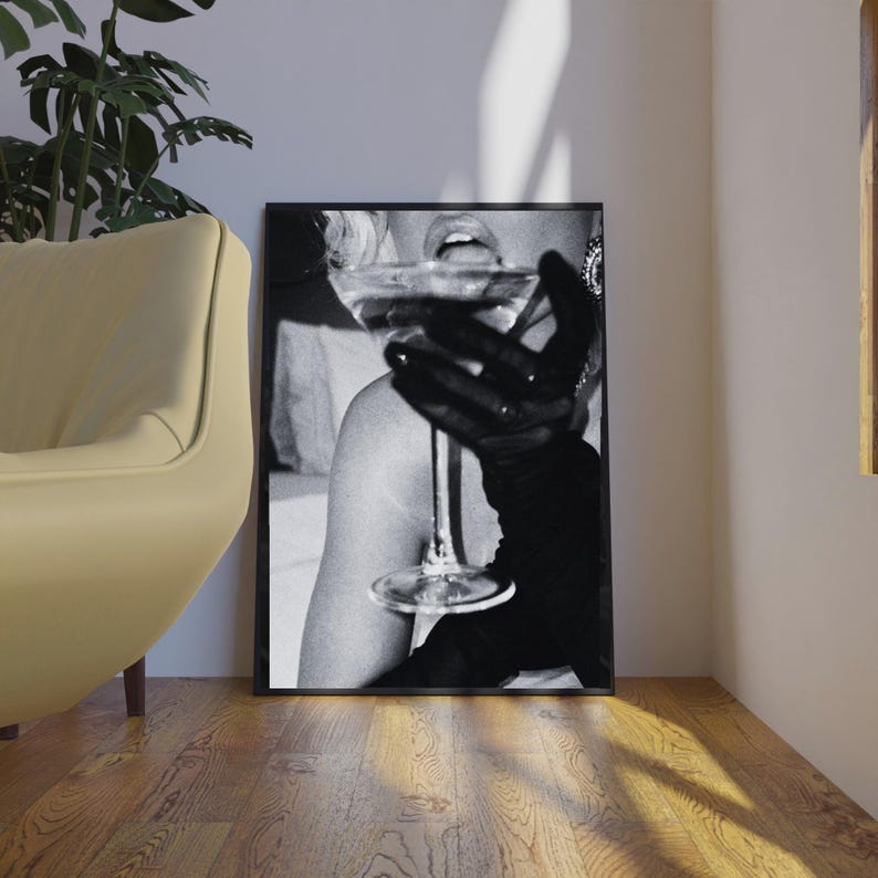 May include: Black and white framed print featuring a person holding a cocktail glass. The person is wearing a black glove. The image is a close-up, with the focus on the glass and the person's mouth.