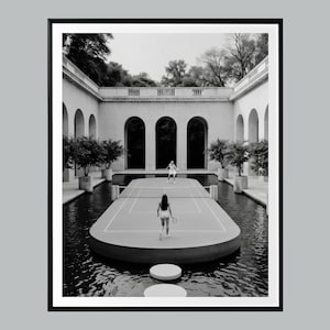 May include: Black and white photograph of a tennis court floating on water. Two people are on the court, one at each end, holding tennis rackets. The court is surrounded by water and a classical building with arches.