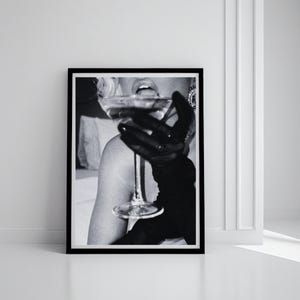 May include: Black and white framed print of a person drinking from a stemmed glass. The person is wearing a black glove. The image is a close-up shot, focusing on the glass and the person's mouth.