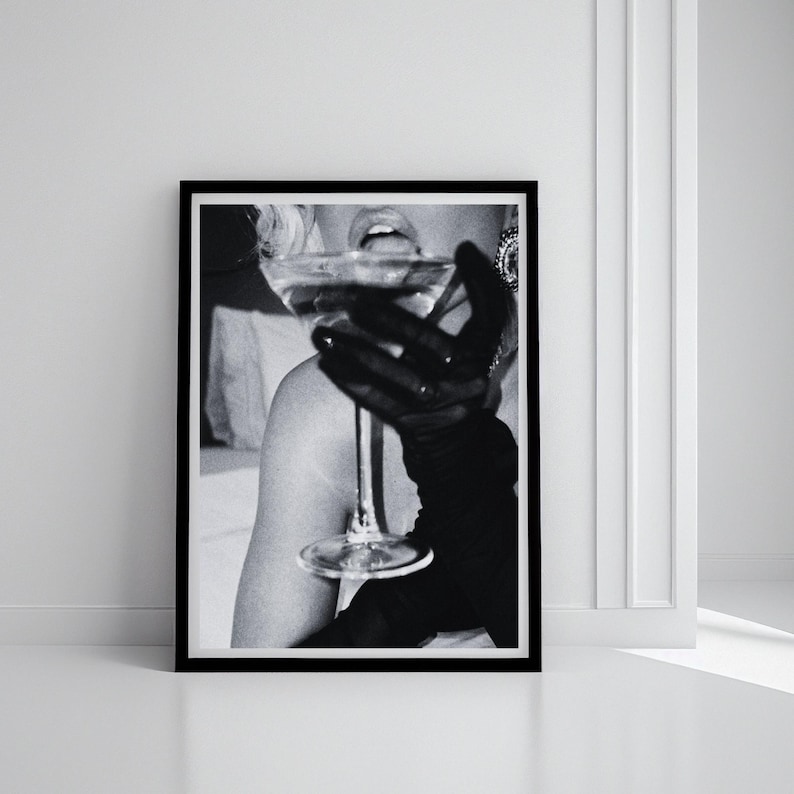 May include: Black and white framed print of a person drinking from a stemmed glass. The person is wearing a black glove. The image is a close-up shot, focusing on the glass and the person's mouth.