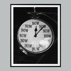 May include: Black and white image of a clock with the word "NOW" repeated around the clock face. The clock hands point to the time of one o'clock. The clock is mounted on a decorative metal bracket.