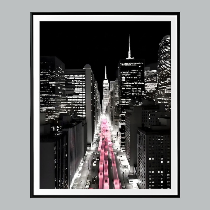 May include: Black and white cityscape print with a pink hue on the road. The image features tall buildings and skyscrapers, with a focus on the city's architecture and urban landscape. The print is framed in a black border.
