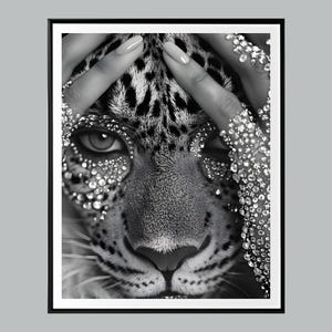 May include: Black and white photograph of a leopard's face with rhinestones covering the eyes and fur. The leopard's face is framed by two hands covered in rhinestones.