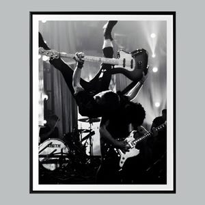 May include: Black and white photograph of a live music performance. Two musicians are upside down, one holding a bass guitar and the other a guitar. A drum set with the word "RUTH" is visible.
