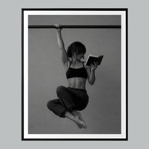 Puede incluir: Fotografía en blanco y negro de una persona leyendo un libro mientras está suspendida de una barra. La persona lleva un sujetador deportivo negro y pantalones oscuros. La imagen está enmarcada en un borde negro.
