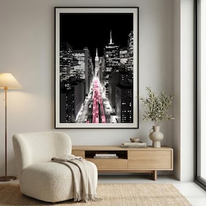 May include: Black and white cityscape photograph with a pink hue down the center. The image features tall buildings and a view down a city street. The photograph is framed in a black border and is displayed on a wall.