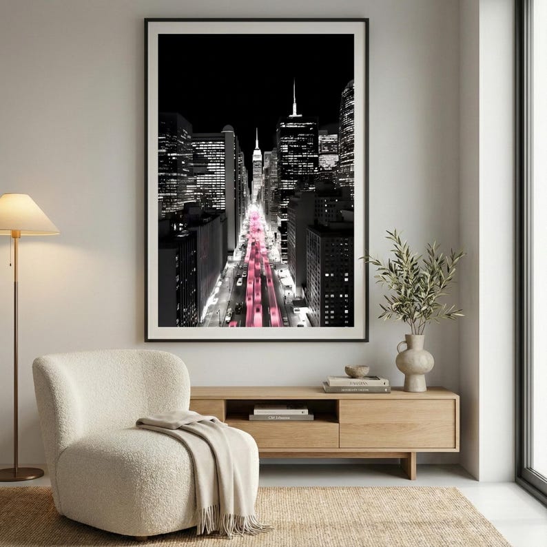 May include: Black and white cityscape photograph with a pink hue down the center. The image features tall buildings and a view down a city street. The photograph is framed in a black border and is displayed on a wall.