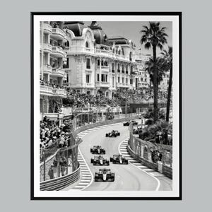 May include: Monochrome framed print depicting a Formula 1 race in Monaco. The image shows race cars on a winding track, with spectators and buildings in the background. Palm trees are also visible.